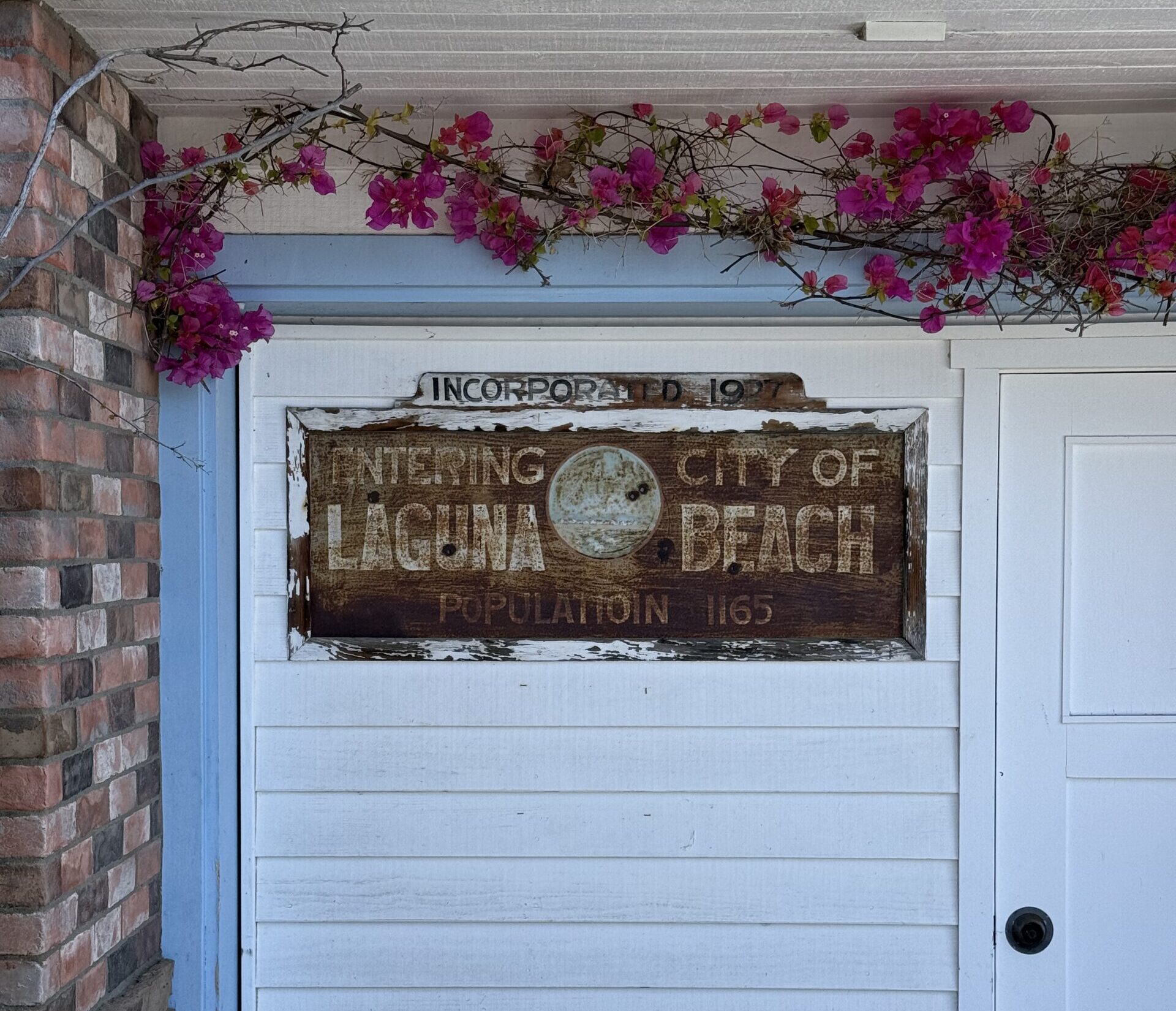 A vintage wooden sign reading "Entering City of Laguna Beach, Incorporated 1927" mounted on a white cottage wall in South Laguna – Representing the neighborhood's deep historical roots.
