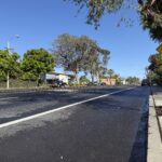Street-level view of South Coast Highway (PCH) in Laguna Beach near the 4th Street intersection, featuring lush trees and a "Signal Ahead" asphalt marking.